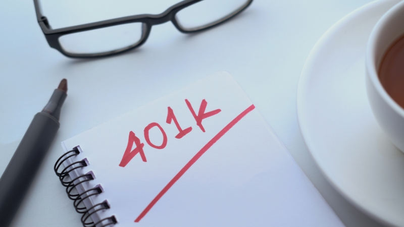 A notebook with "401K" written on it next to glasses, a pen, and coffee