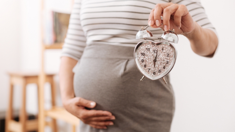 Pregnant woman holds a clock to show timing of maternity leave in the US