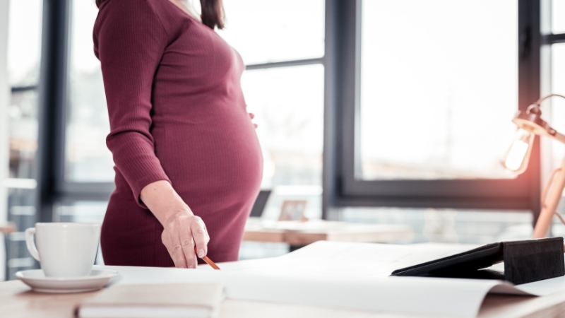 Pregnant woman stands at a desk reviewing documents during maternity leave planning